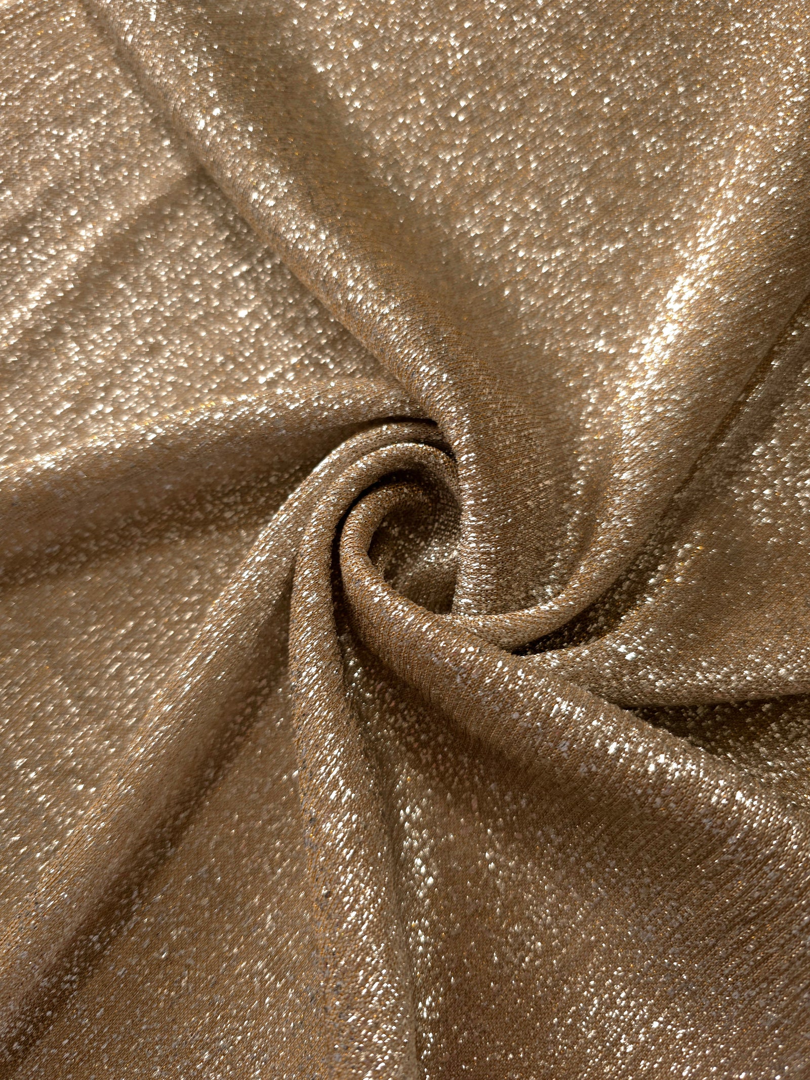 Swirl-draped Antique Gold Sheer Glitter Stretch Tulle Fabric capturing reflective sparkle and fluid movement through flexible folds