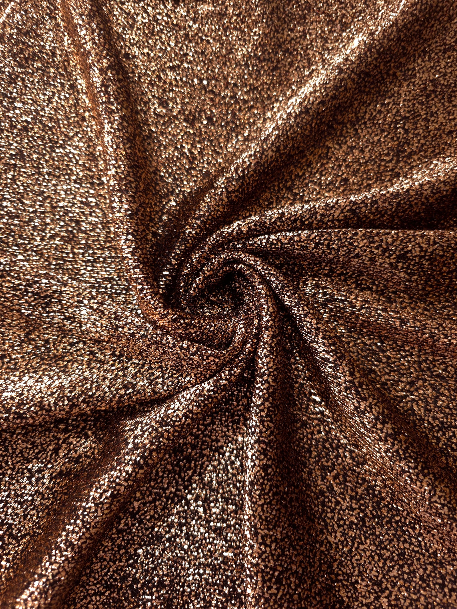 Swirl-draped Copper Bronze Sheer Glitter Stretch Tulle Fabric capturing reflective sparkle and fluid movement through flexible folds