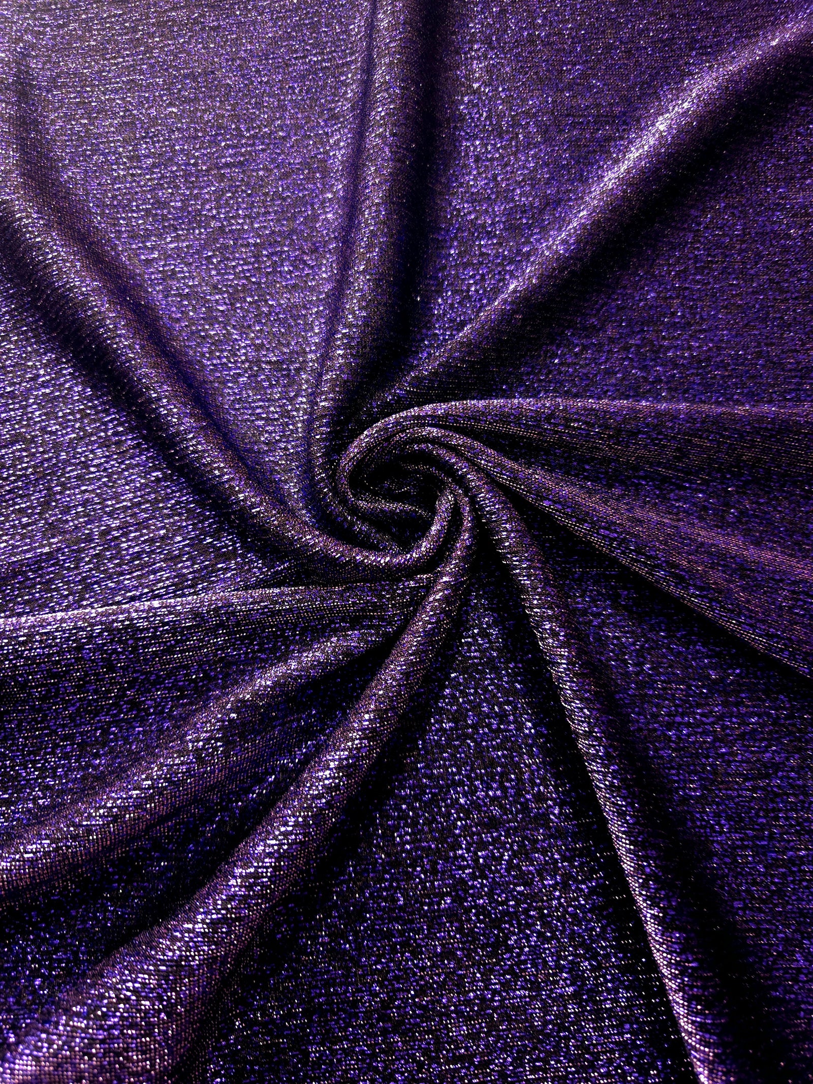 Swirl-draped Deep Violet Sheer Glitter Stretch Tulle Fabric capturing reflective sparkle and fluid movement through flexible folds