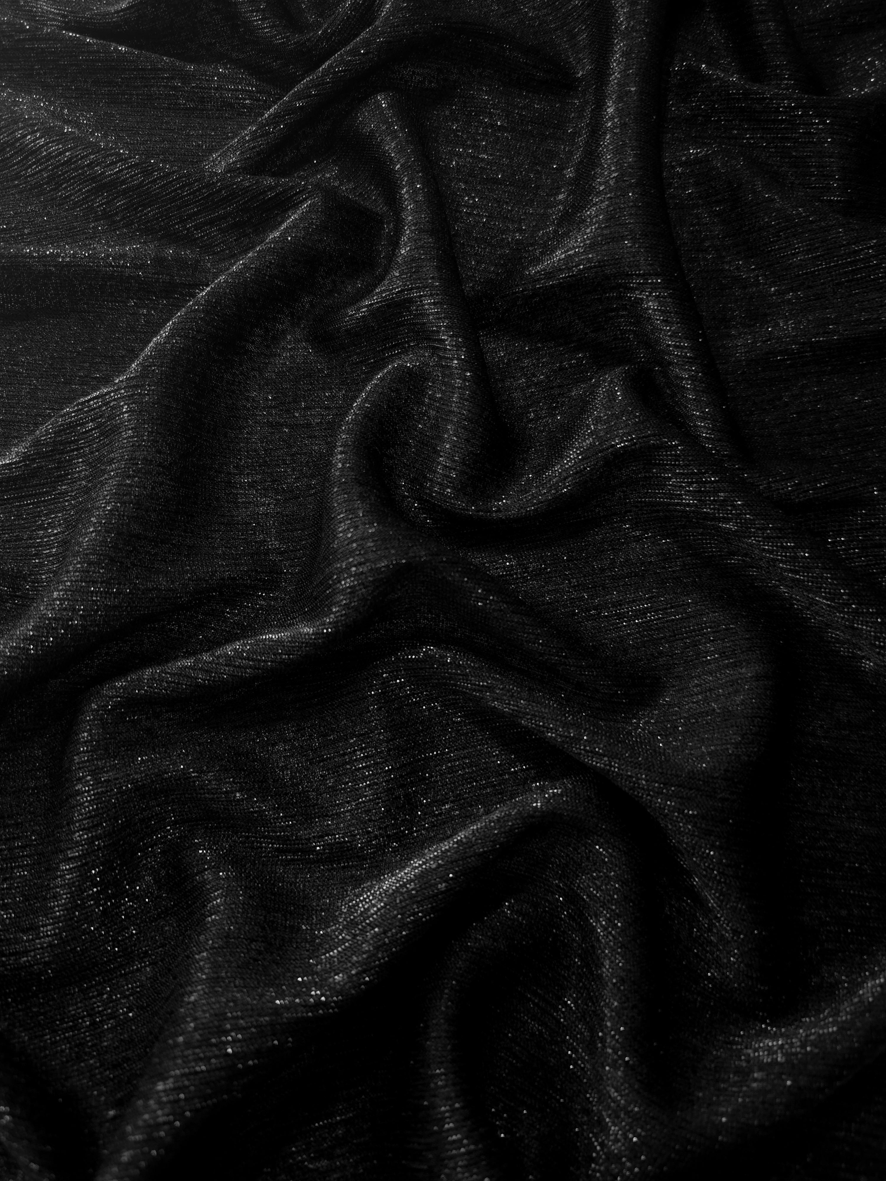 Draped Jet Black Sheer Glitter Stretch Tulle Fabric showing scattered sparkle across fluid folds for eveningwear and stage looks