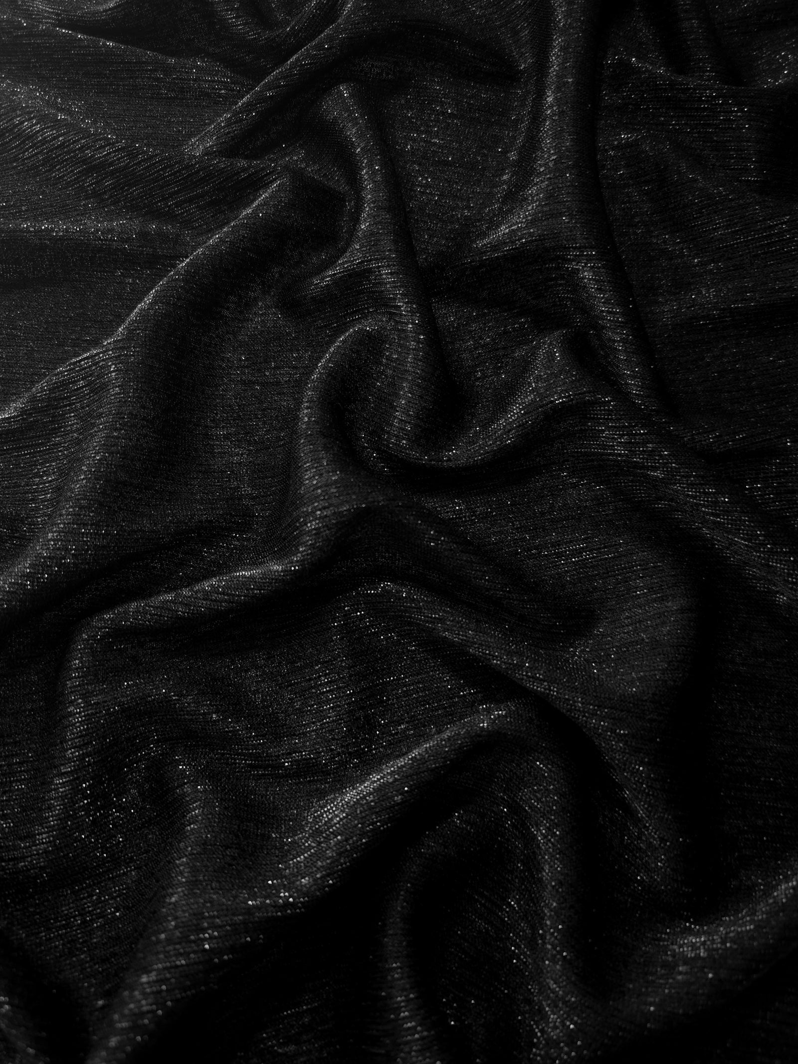 Draped Jet Black Sheer Glitter Stretch Tulle Fabric showing scattered sparkle across fluid folds for eveningwear and stage looks