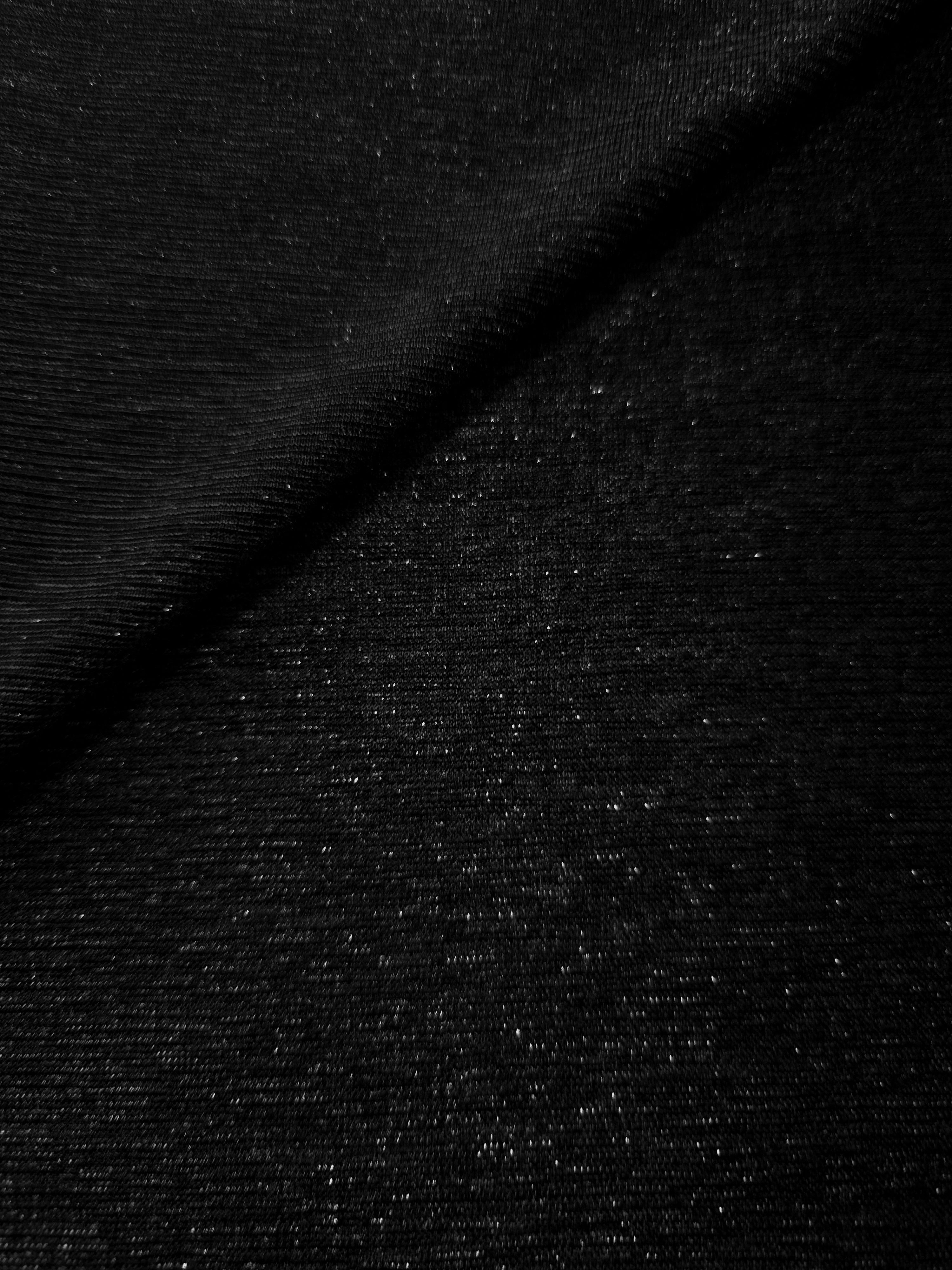 Front and back of Jet Black Sheer Glitter Stretch Tulle Fabric showing transparent knit construction and flexible 4-way stretch