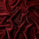 Draped Ruby Red Sheer Glitter Stretch Tulle Fabric showing scattered sparkle across fluid folds for eveningwear and stage looks