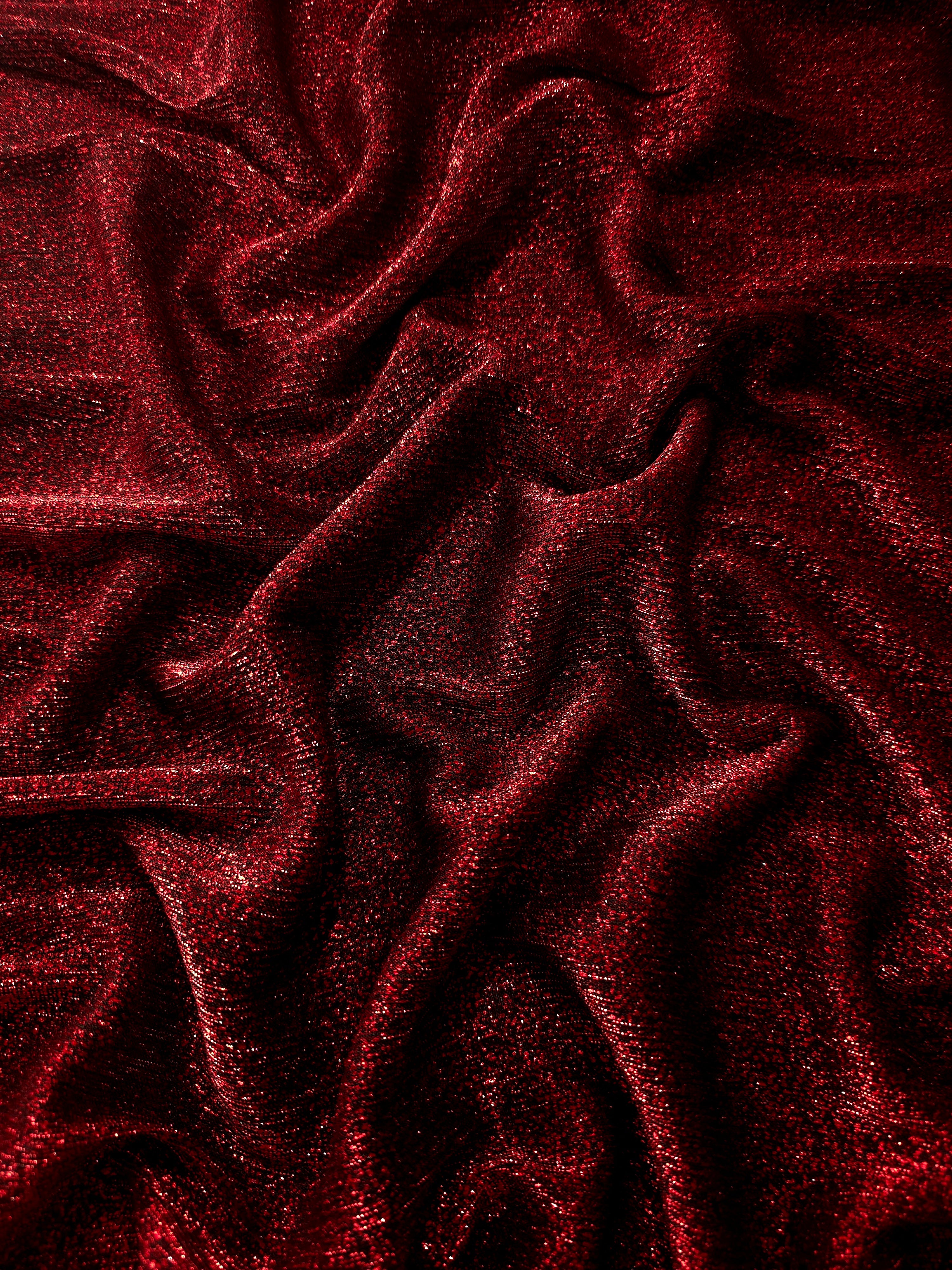 Draped Ruby Red Sheer Glitter Stretch Tulle Fabric showing scattered sparkle across fluid folds for eveningwear and stage looks