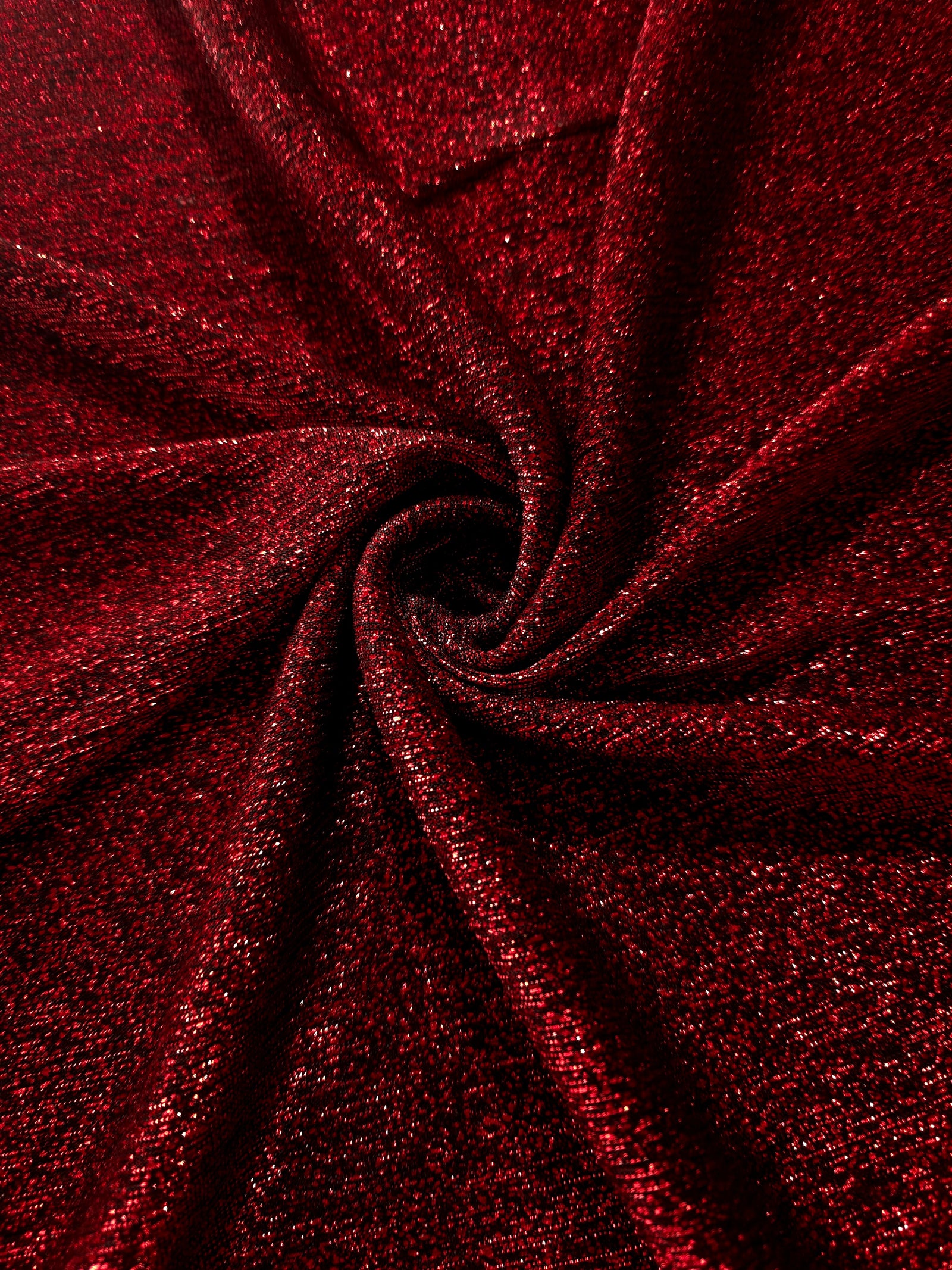 Swirl-draped Ruby Red Sheer Glitter Stretch Tulle Fabric capturing reflective sparkle and fluid movement through flexible folds