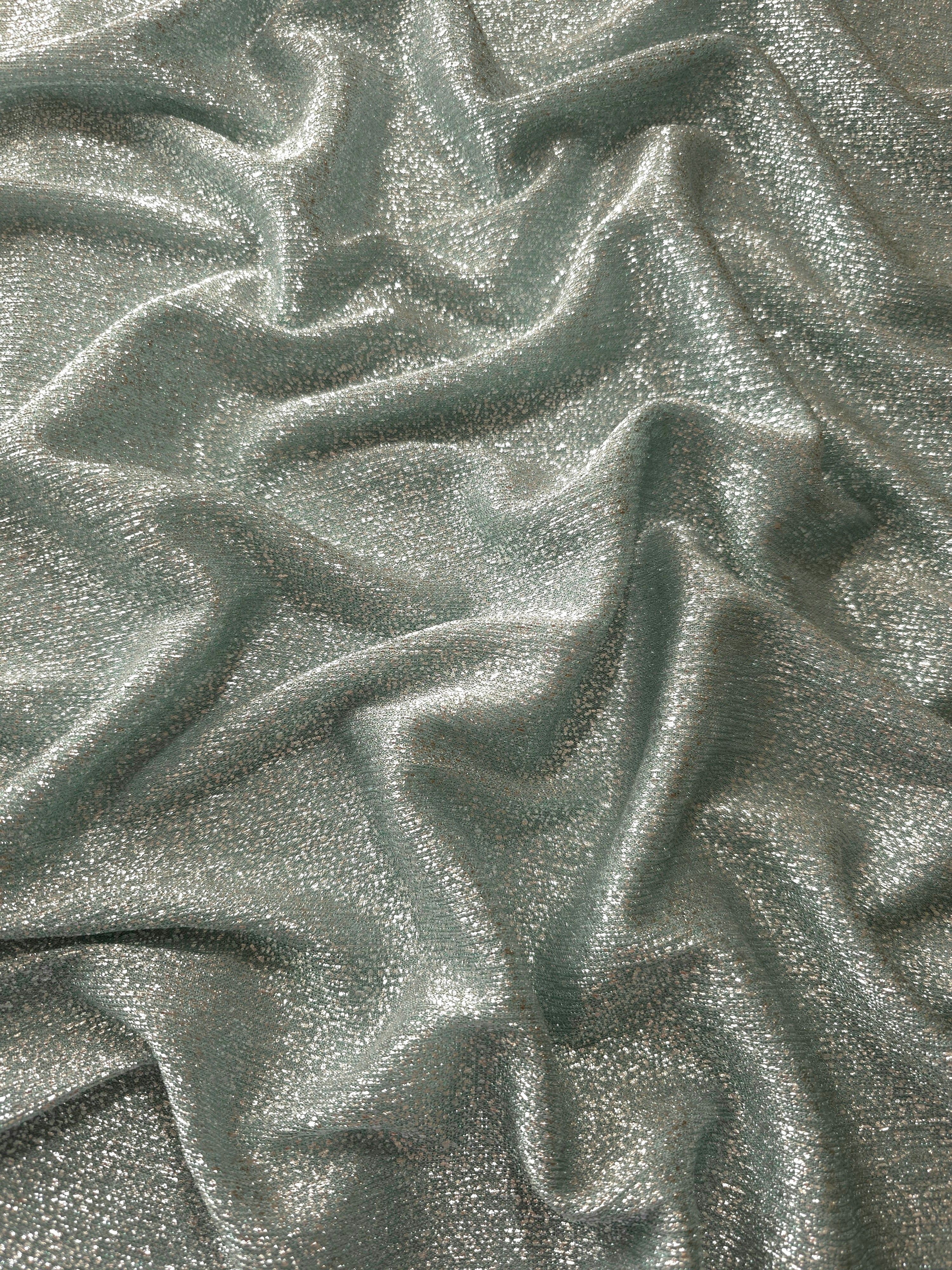 Draped Silver Sage Sheer Glitter Stretch Tulle Fabric showing scattered sparkle across fluid folds for eveningwear and stage looks