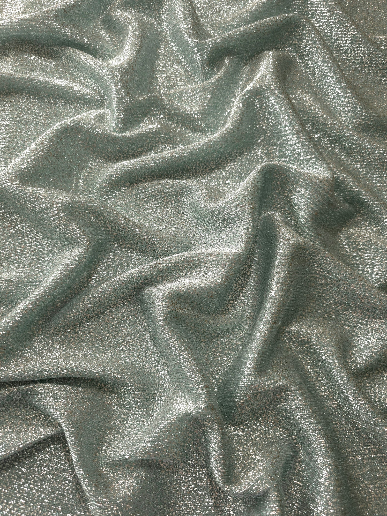 Draped Silver Sage Sheer Glitter Stretch Tulle Fabric showing scattered sparkle across fluid folds for eveningwear and stage looks