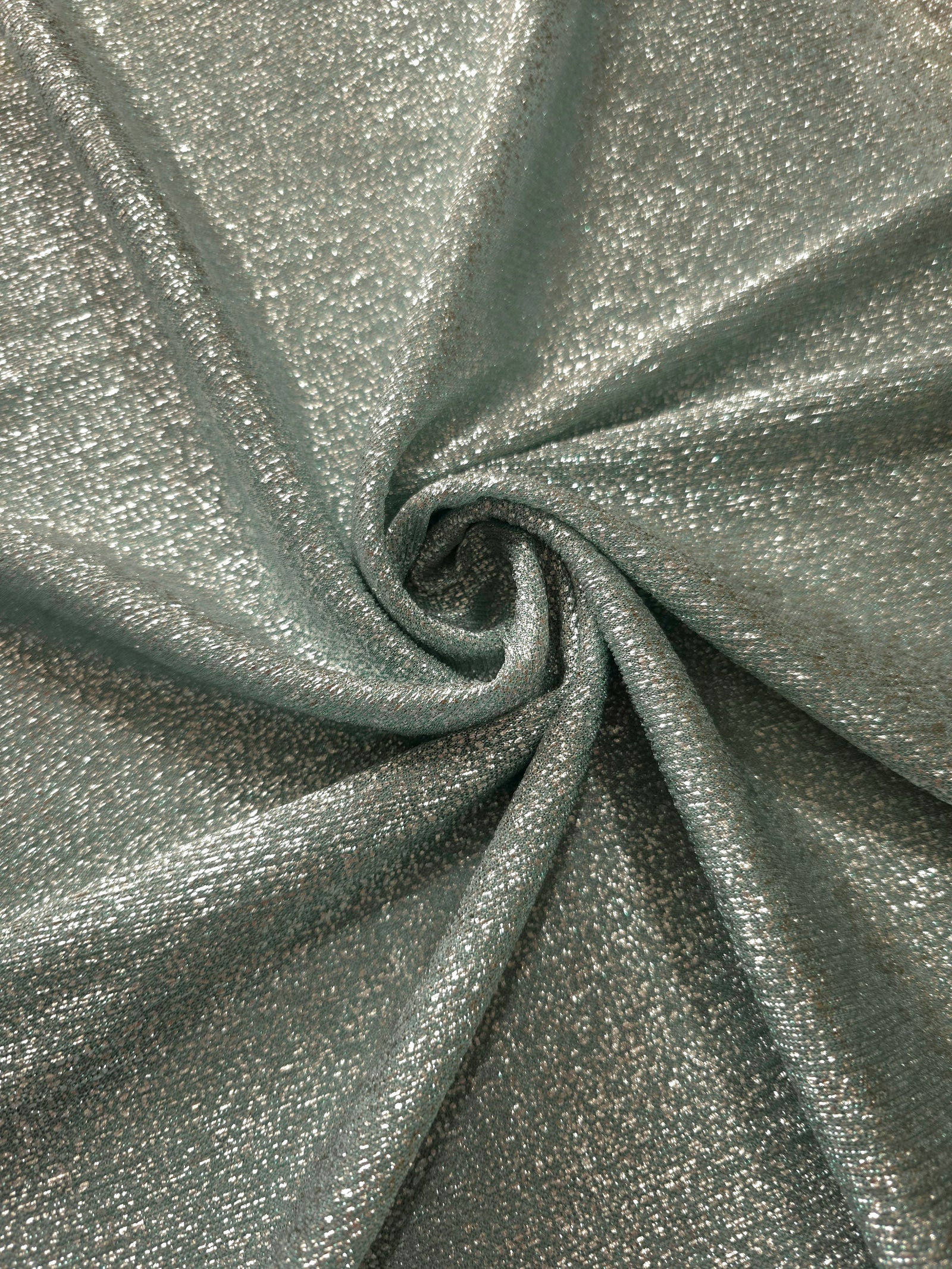 Swirl-draped Silver Sage Sheer Glitter Stretch Tulle Fabric capturing reflective sparkle and fluid movement through flexible folds