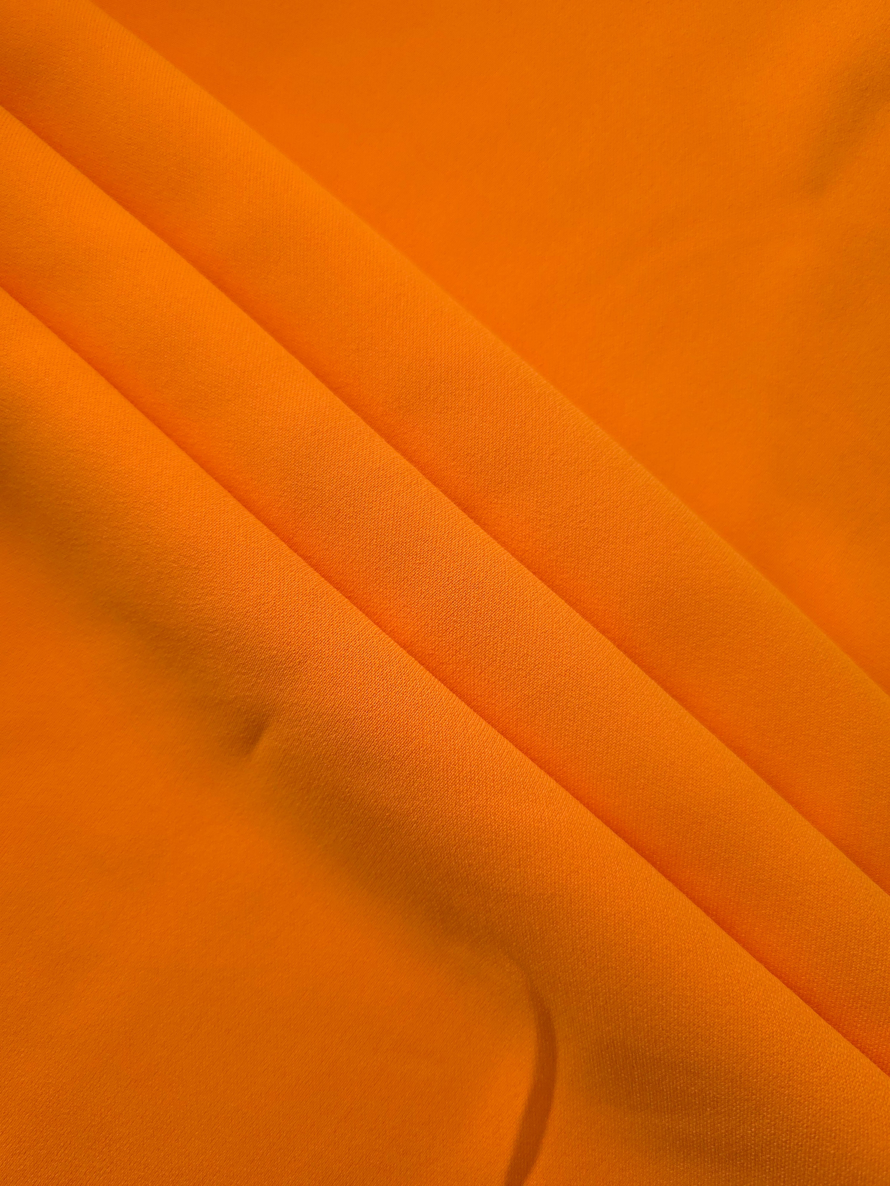 Layered Tangerine Orange polyester crepe showing soft body and gentle mechanical stretch for dressmaking