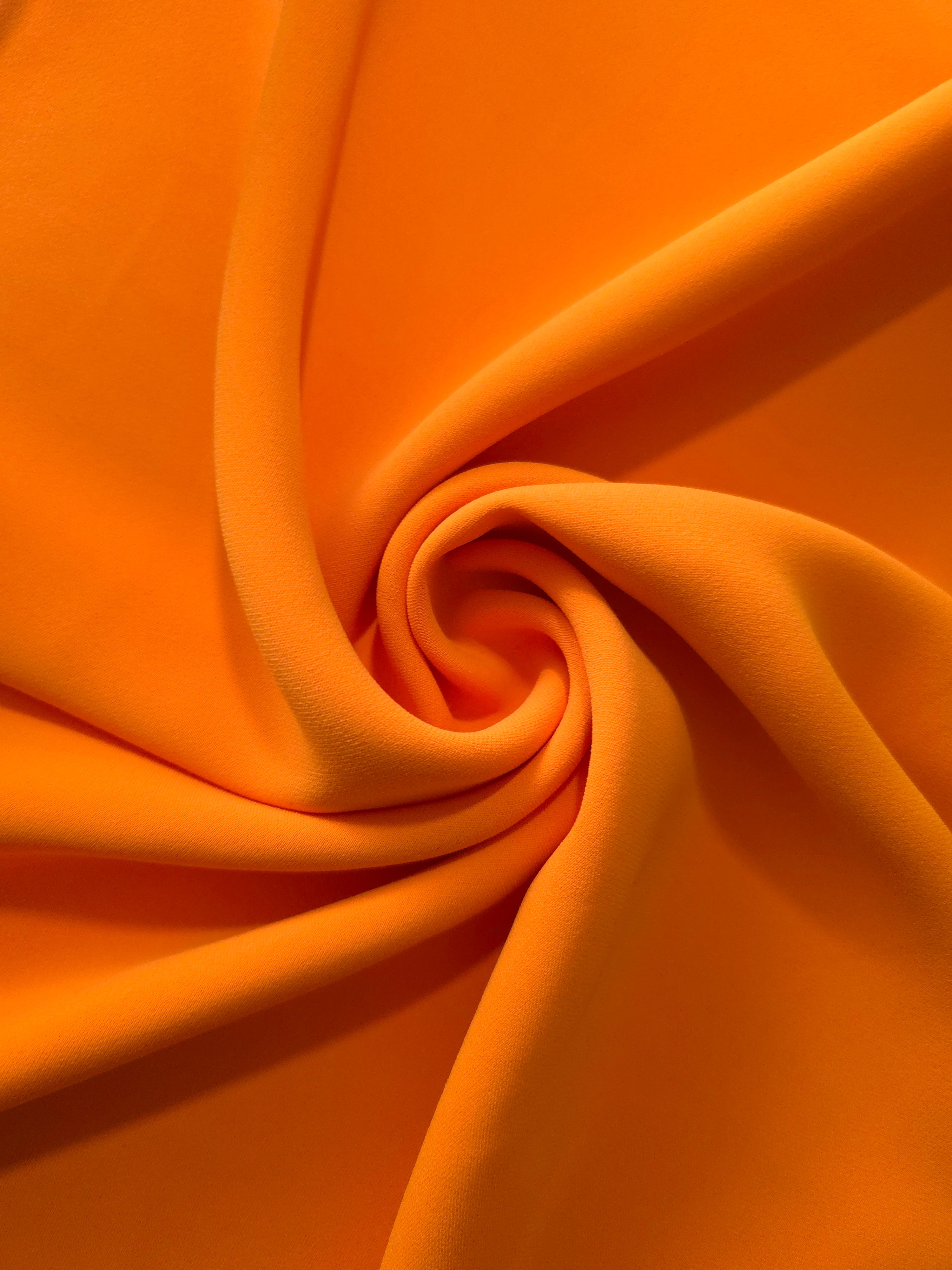 Circular drape of Tangerine Orange polyester crepe showing flowing movement for occasion dresses and modest fashion