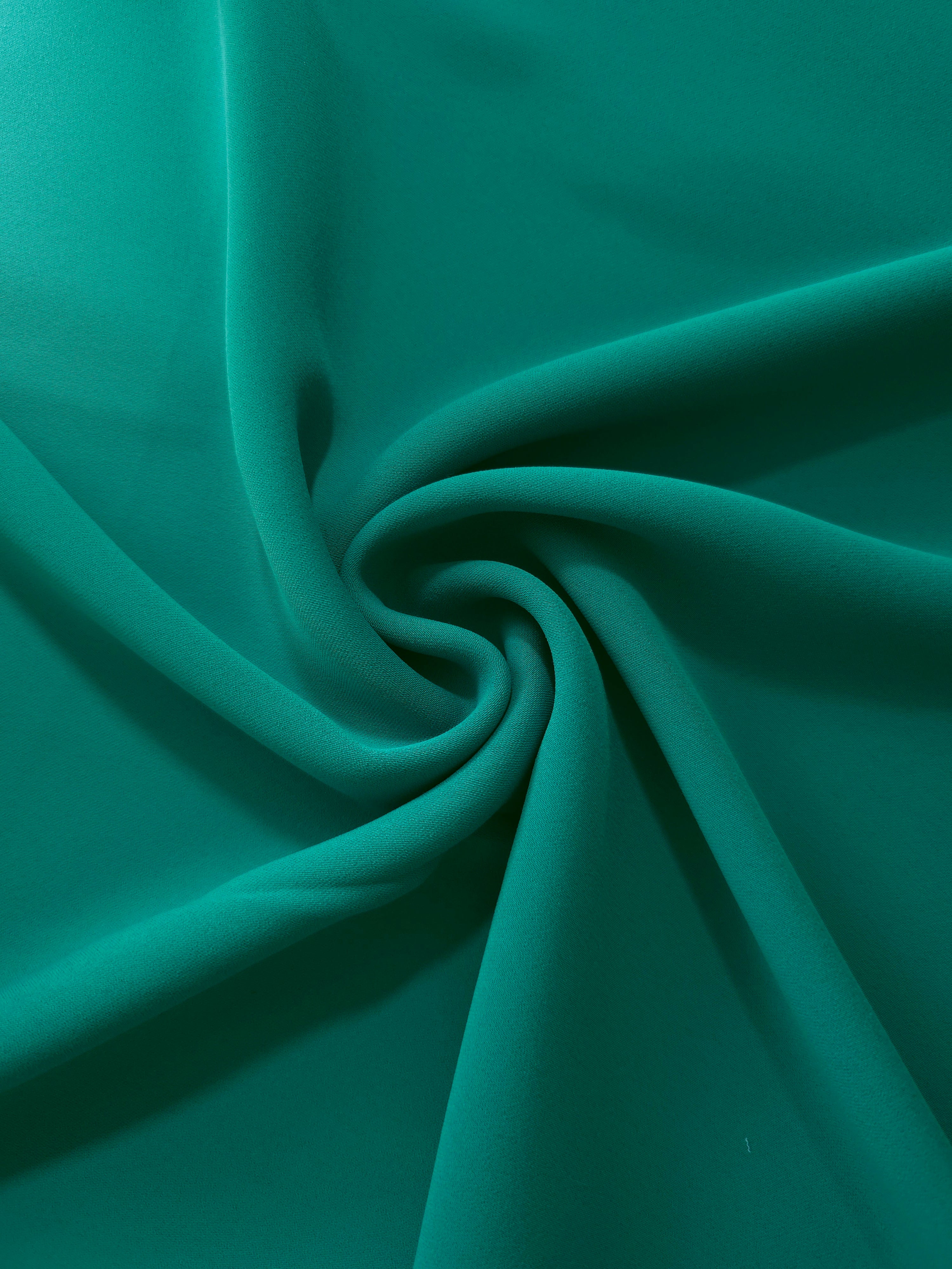 Flowing swirl of Teal Green polyester crepe showing soft movement for blouses, dresses and abayas