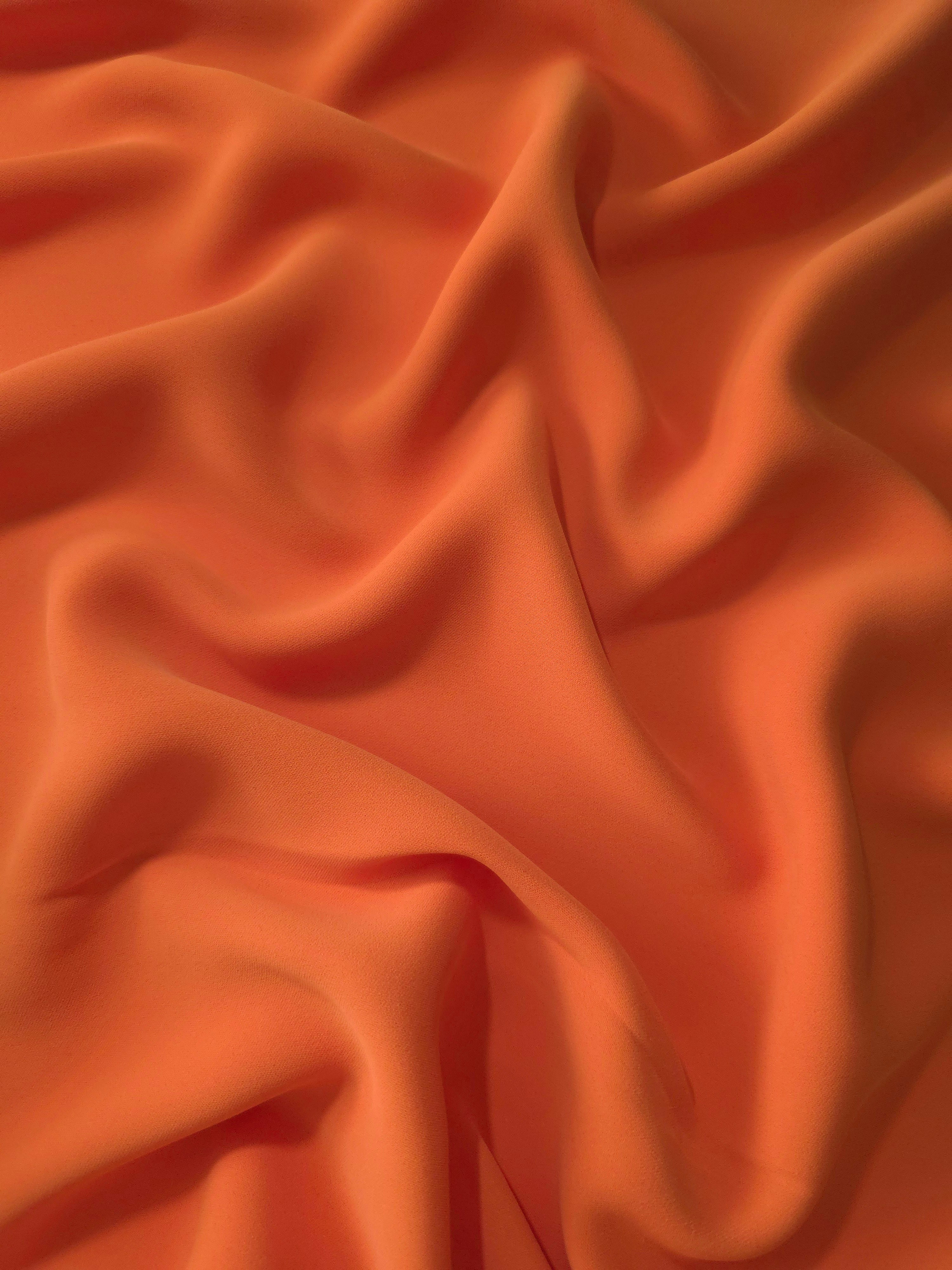 Draped folds of Terracotta Orange polyester crepe showing fluid movement for dresses, skirts and elegant apparel