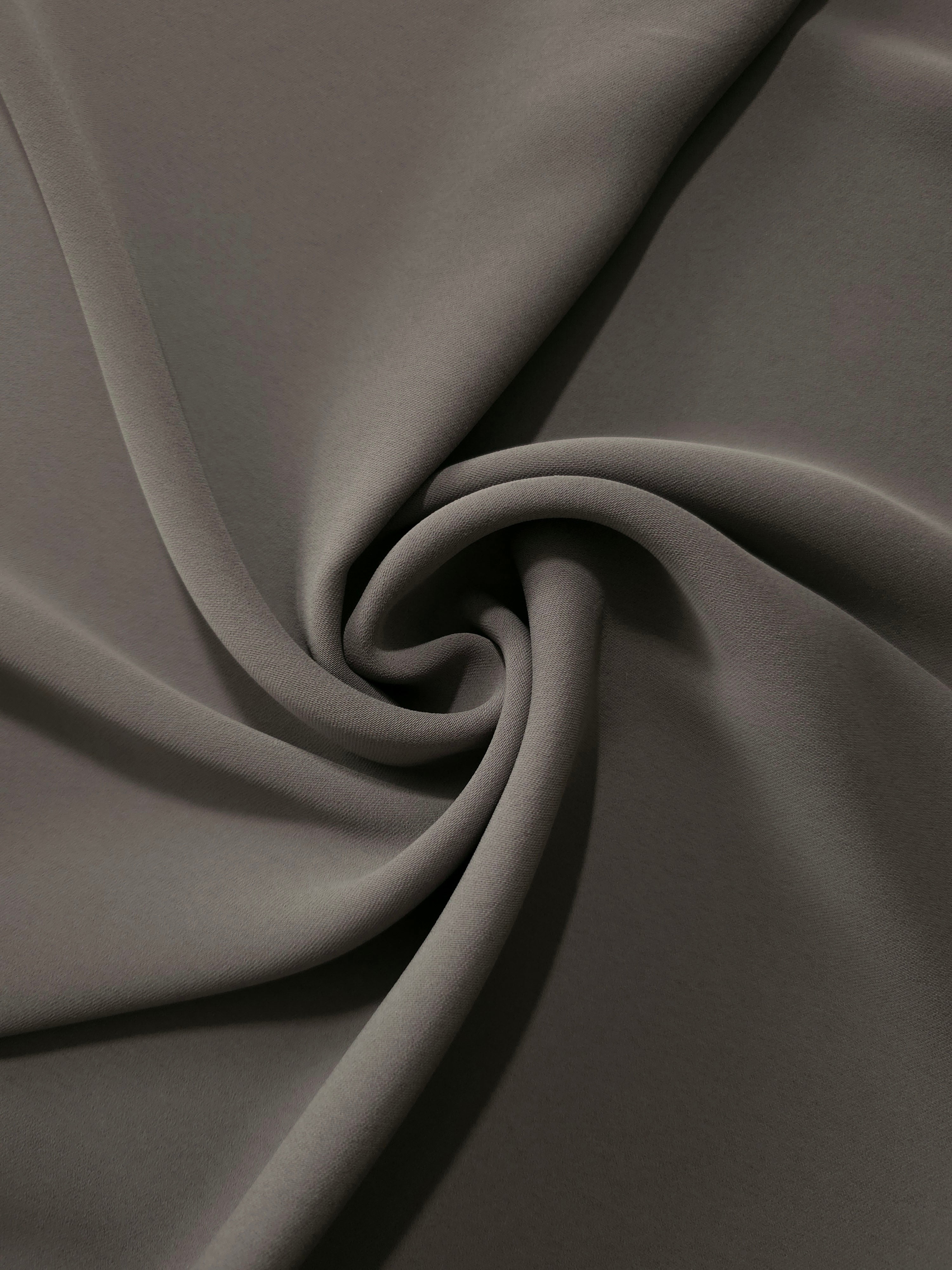 Warm Charcoal Gray polyester crepe arranged in a flowing swirl, showing drape used for abayas and modest fashion