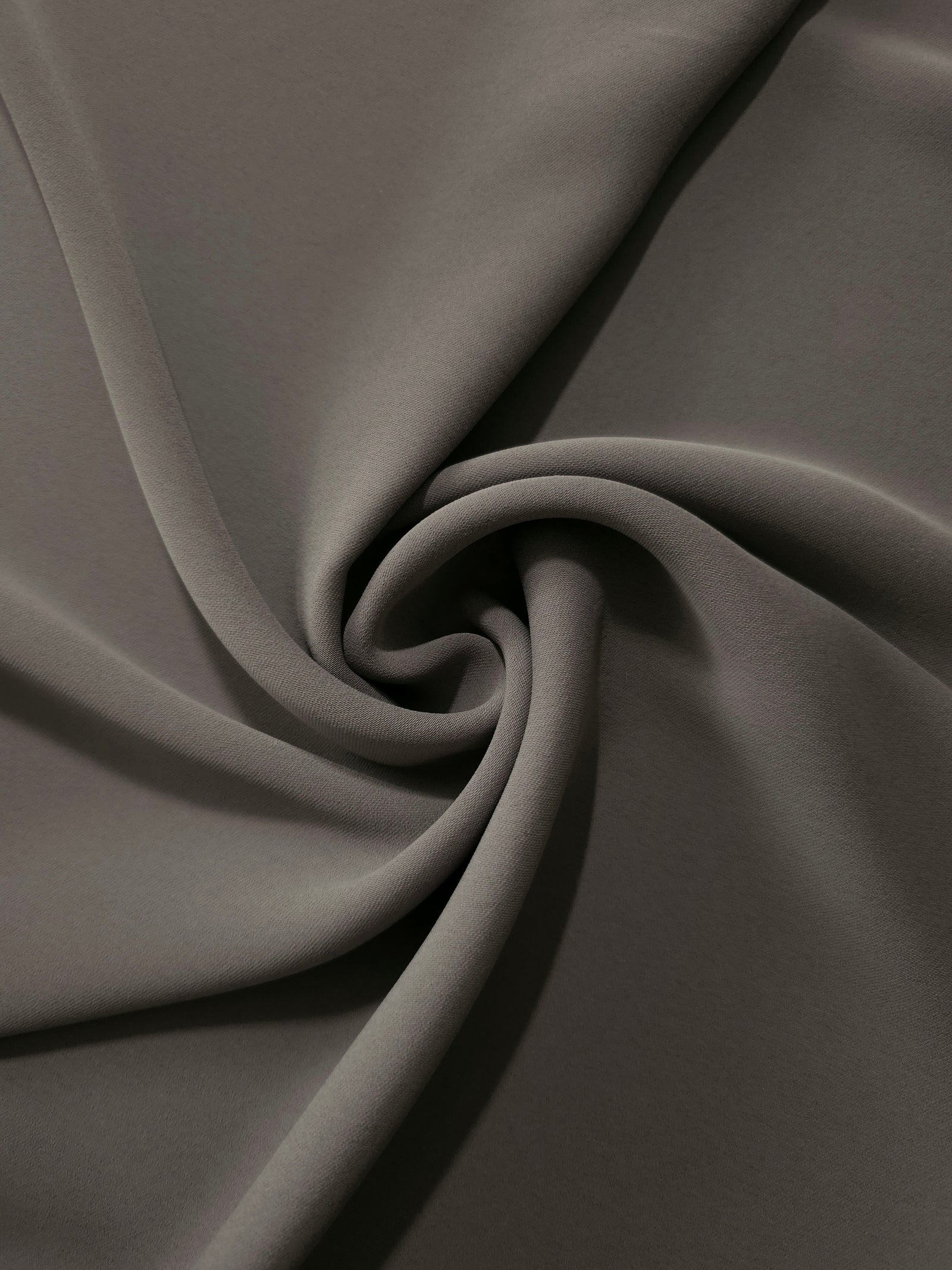 Warm Charcoal Gray polyester crepe arranged in a flowing swirl, showing drape used for abayas and modest fashion