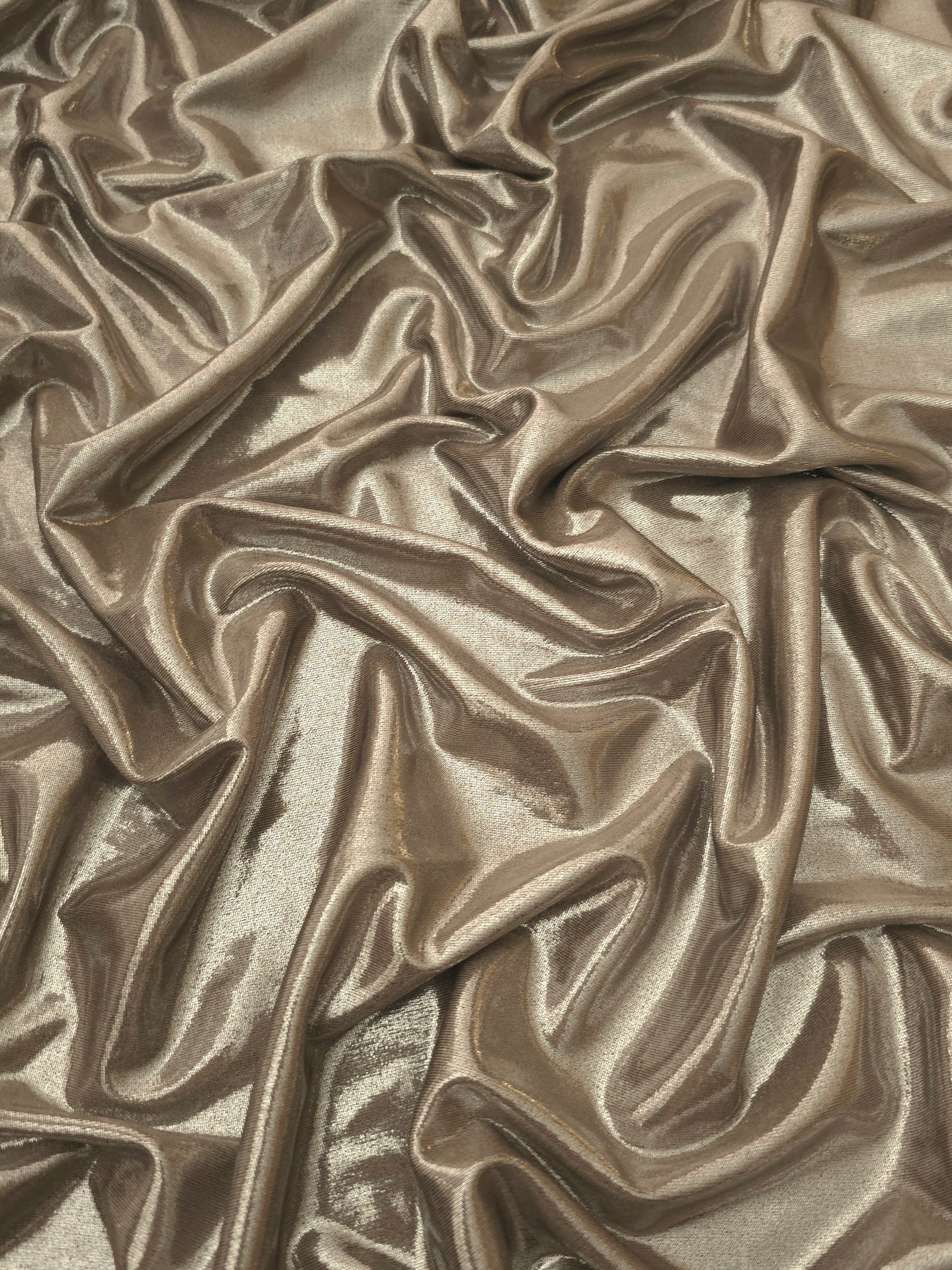 Draped Warm Greige Beige metallic foiled spandex showing reflective folds and flexible flow for dresses, stagewear and occasion looks