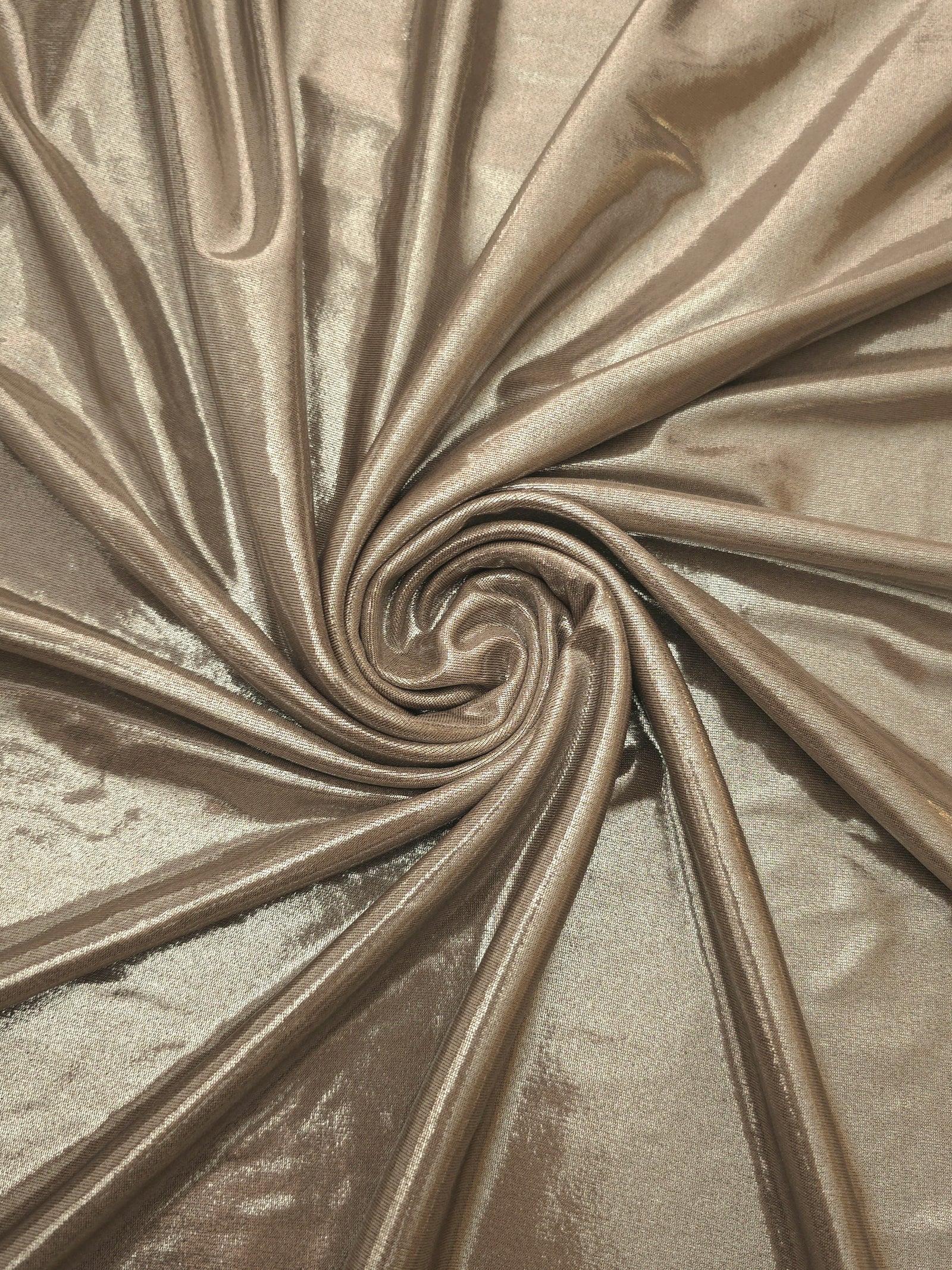 Warm Greige Beige shimmer foiled stretch fabric arranged in a swirl, highlighting movement and reflective finish for performancewear