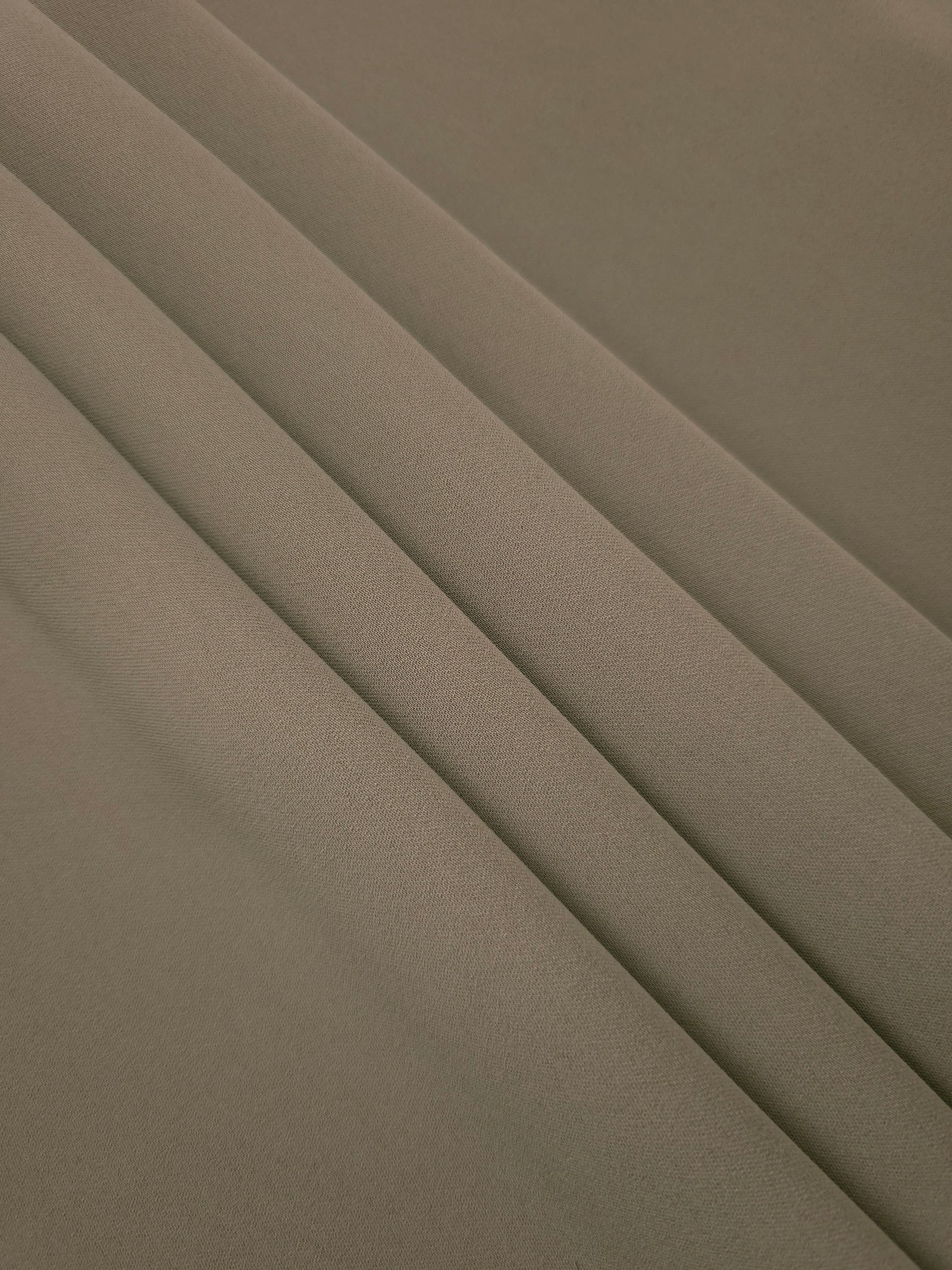 Layered folds of Warm Stone Taupe 100% mechanical polyester crepe showing body and gentle construction stretch