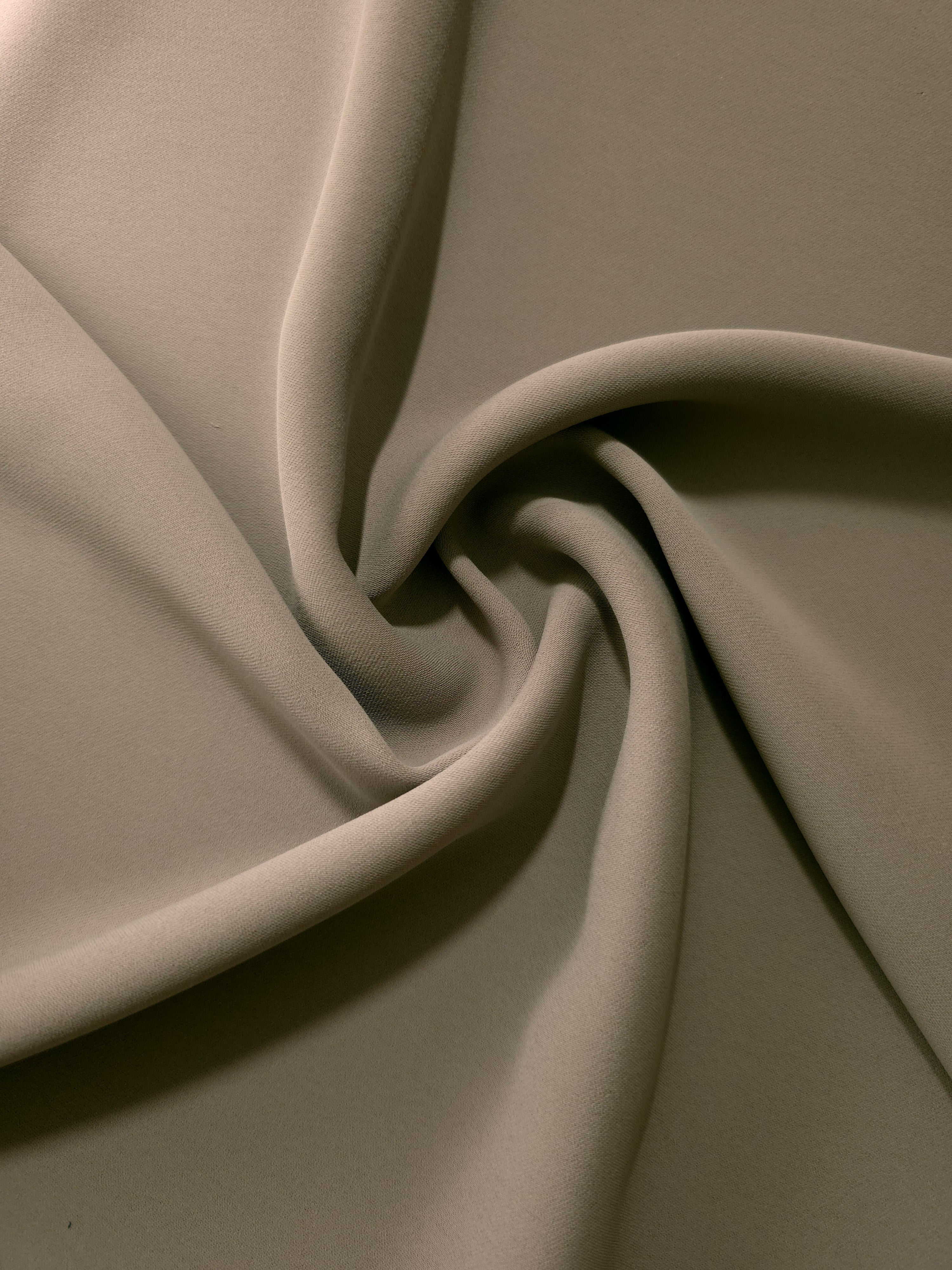 Warm Stone Taupe opaque polyester crepe in a spiral drape, showing flowing form for skirts and modest garments