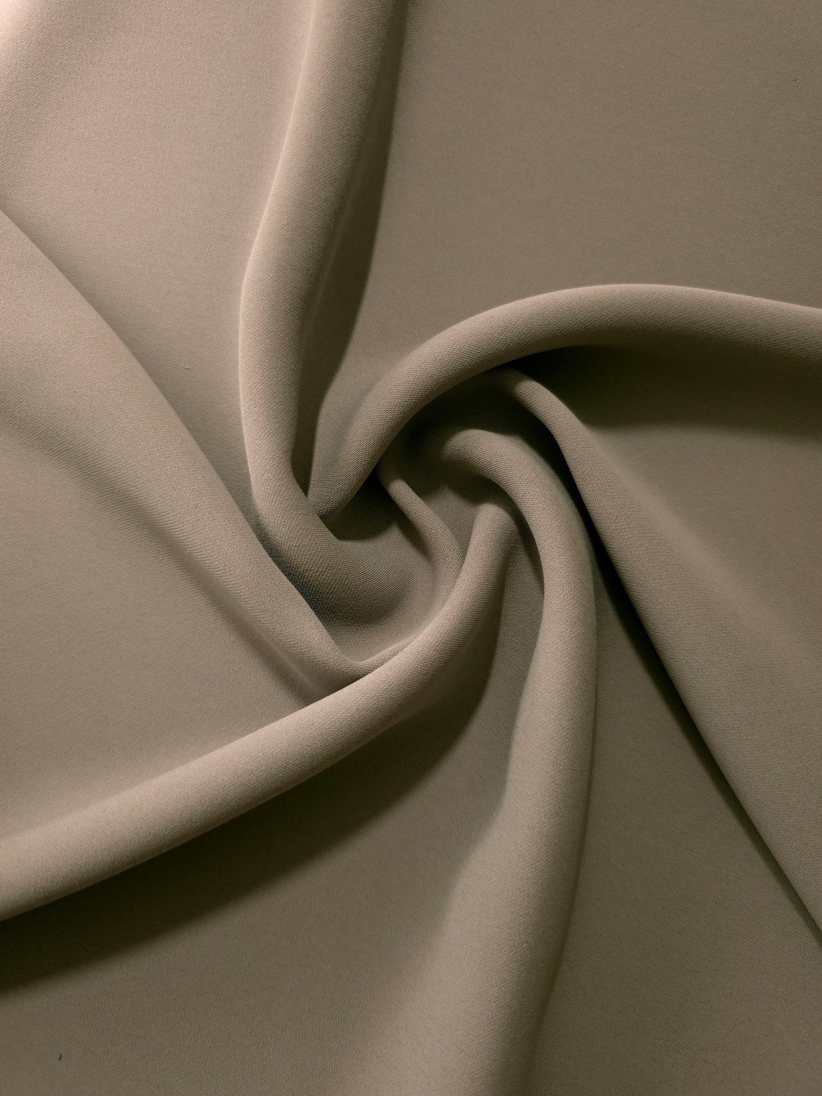 Warm Stone Taupe opaque polyester crepe in a spiral drape, showing flowing form for skirts and modest garments