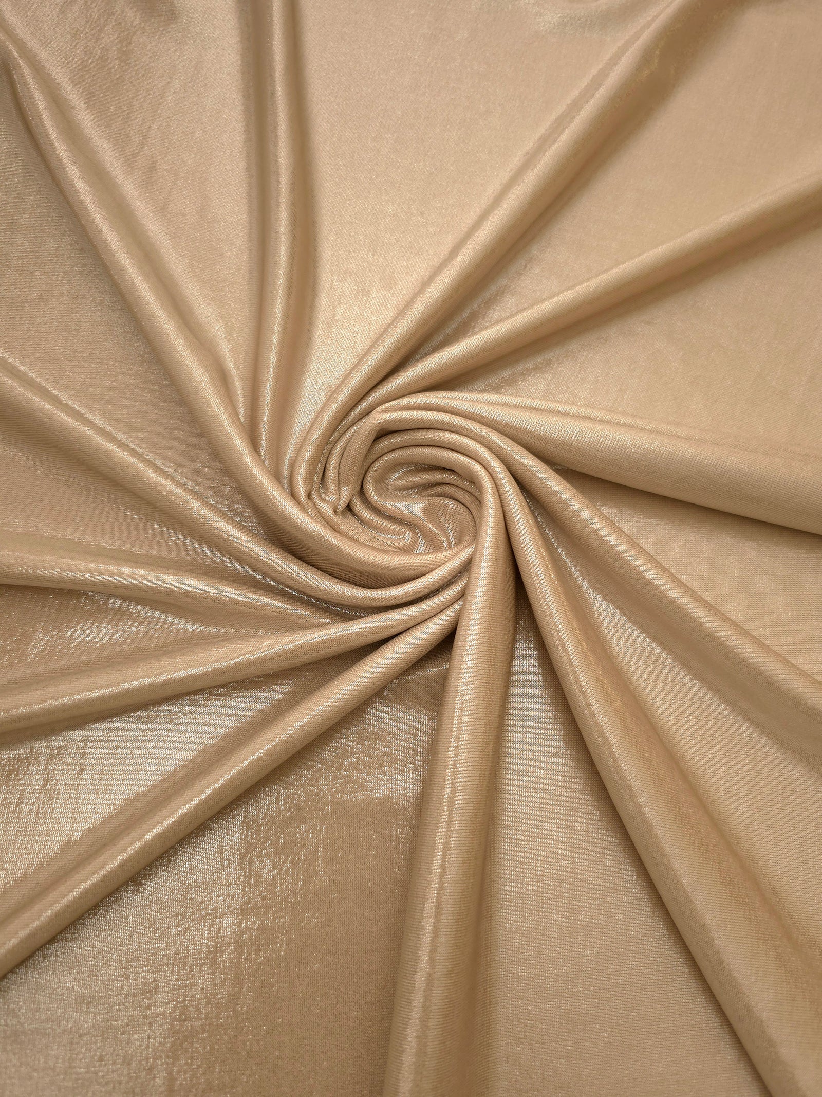 Warm Taupe Beige shimmer foiled stretch fabric arranged in a swirl, highlighting movement and reflective finish for performancewear